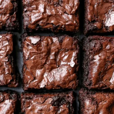 Fudgiest brownies topped with chocolate icing on a wooden table